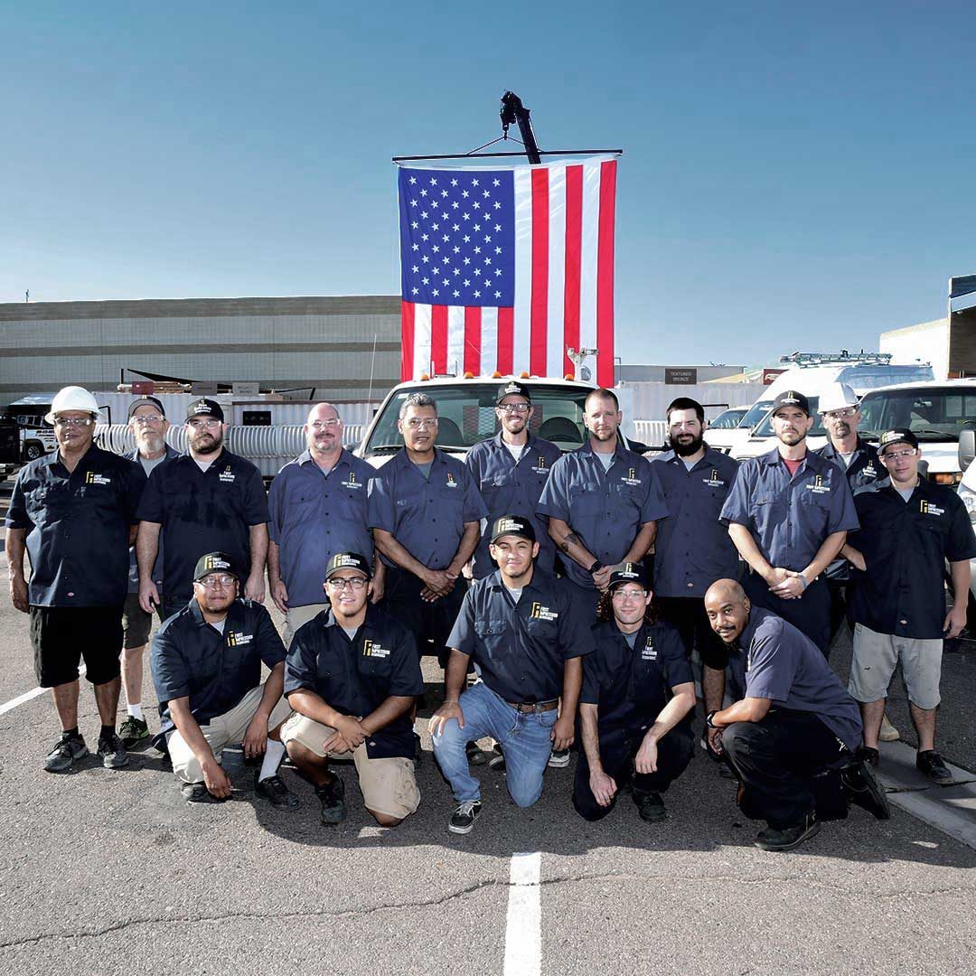 Group of First Impression Ironworks Employees With Flag Behind Them