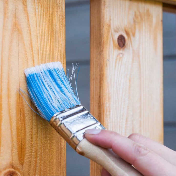 Hand Holding a Brush Painting Sealant on Redwood