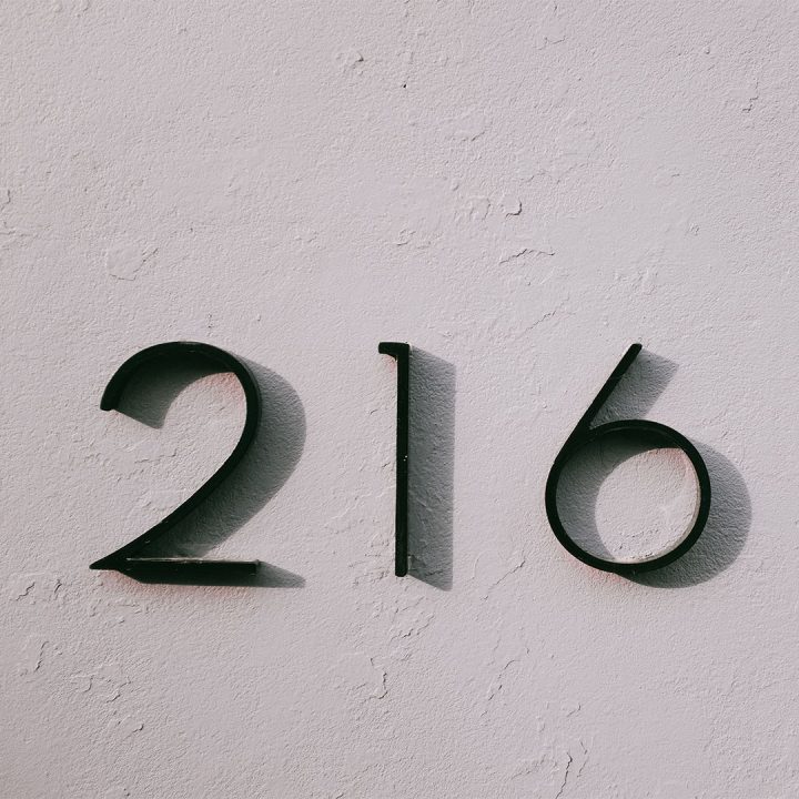 Black home address numbers (216) on an outdoor white wall