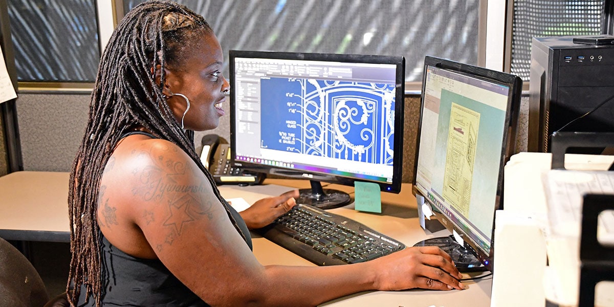 1st Impression Ironworks CAD Designer working on her computer at her desk.  Our iron entry doors and iron security doors can be delivered nationwide.