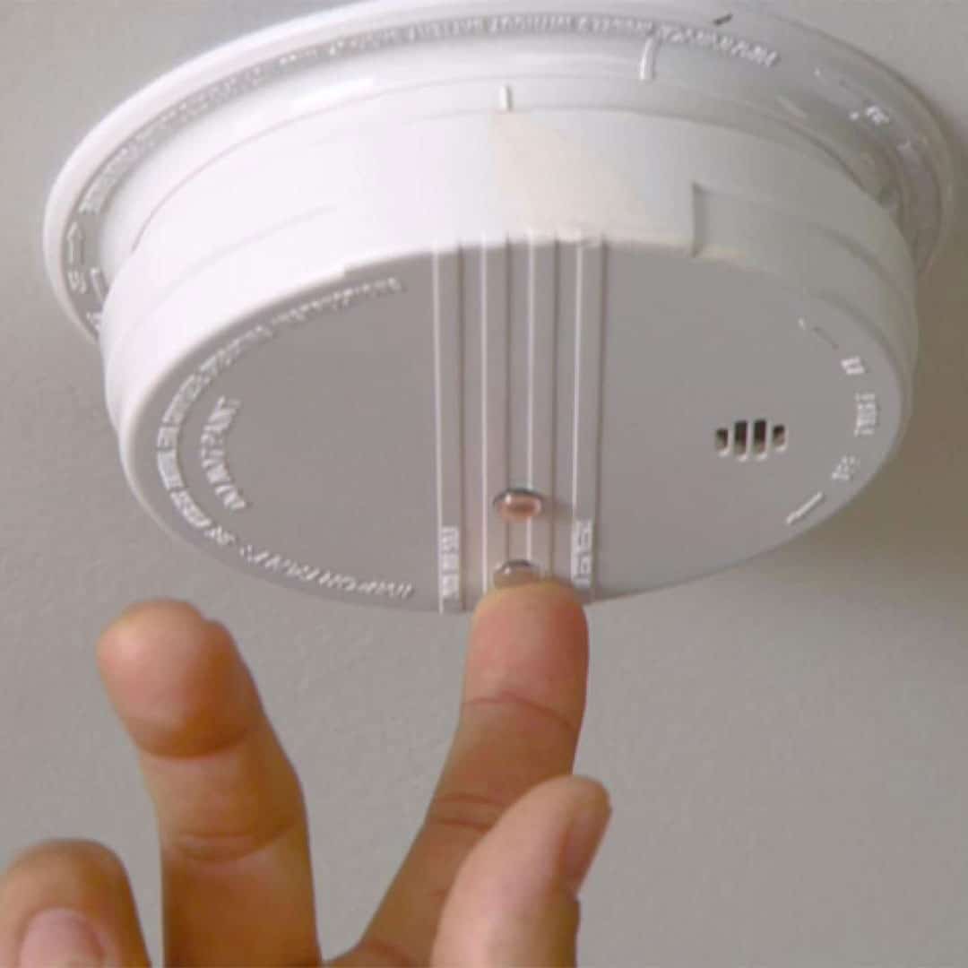 finger pressing the button on a smoke detector to test that it is working properly