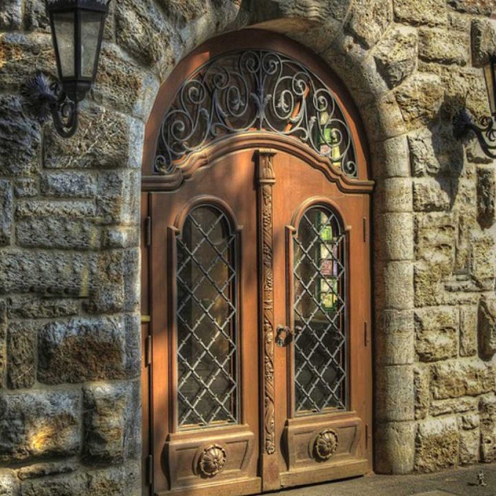 large arched wooden and glass door surrounded by an old stone building