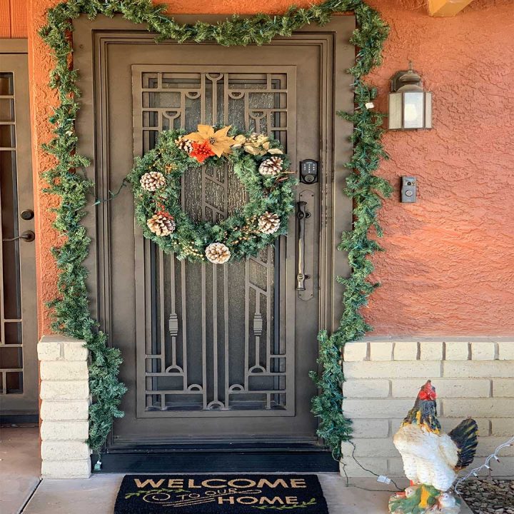 First Impression Ironworks Iron Entry Door with a large wreath hanging from it.  Door is surrounded by holiday garland