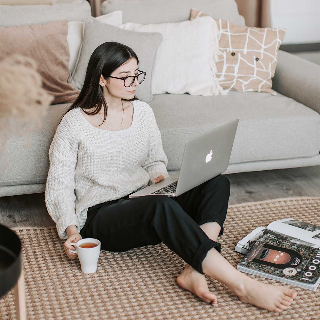 young woman drinking coffee while looking at a laptop