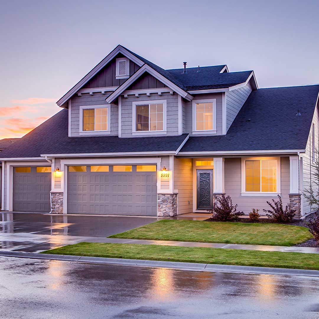 The front of a home, with outdoor and indoor lights on, as the sun is setting