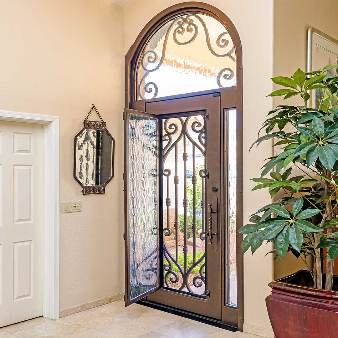 large arched Tuscan iron entry door with glass panel that is open to allow airflow