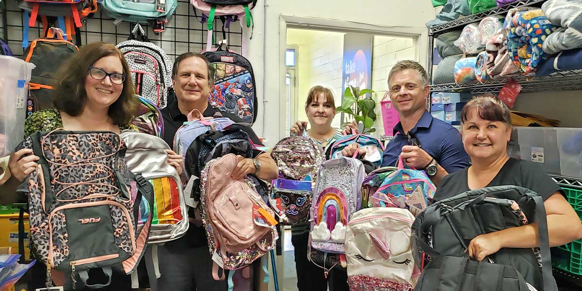 First Impression Ironworks team members holding up backpacks at Backpacks 4 Kids AZ