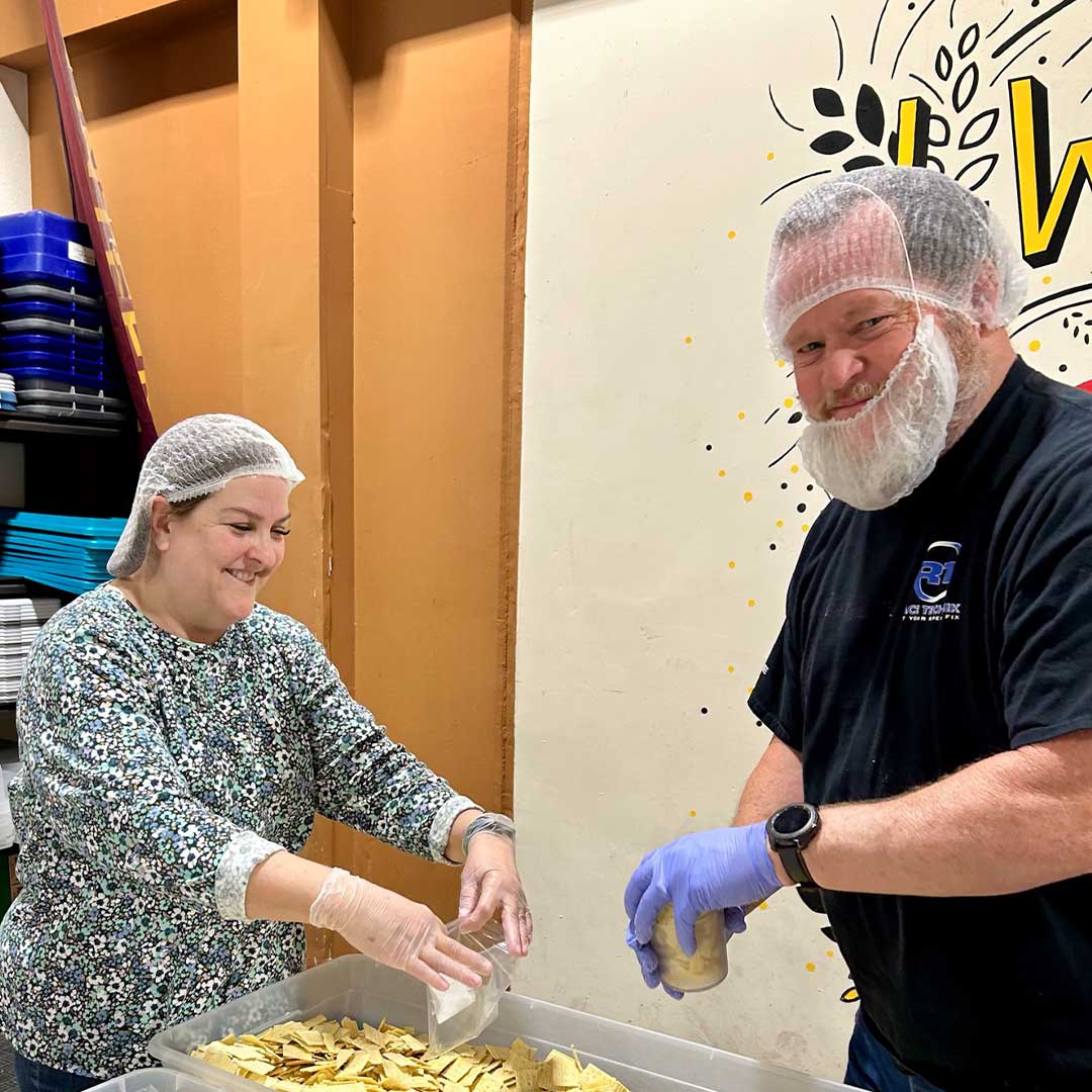 Two First Impression Ironworks employees packing crackers into small serving bags at Midwest Food Bank