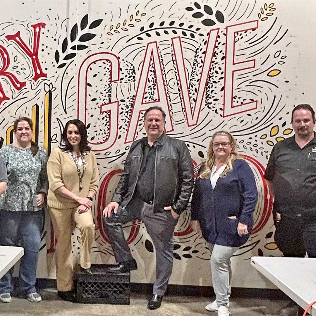 First Impression Ironworks team standing in front of a mural at Midwest Food Bank