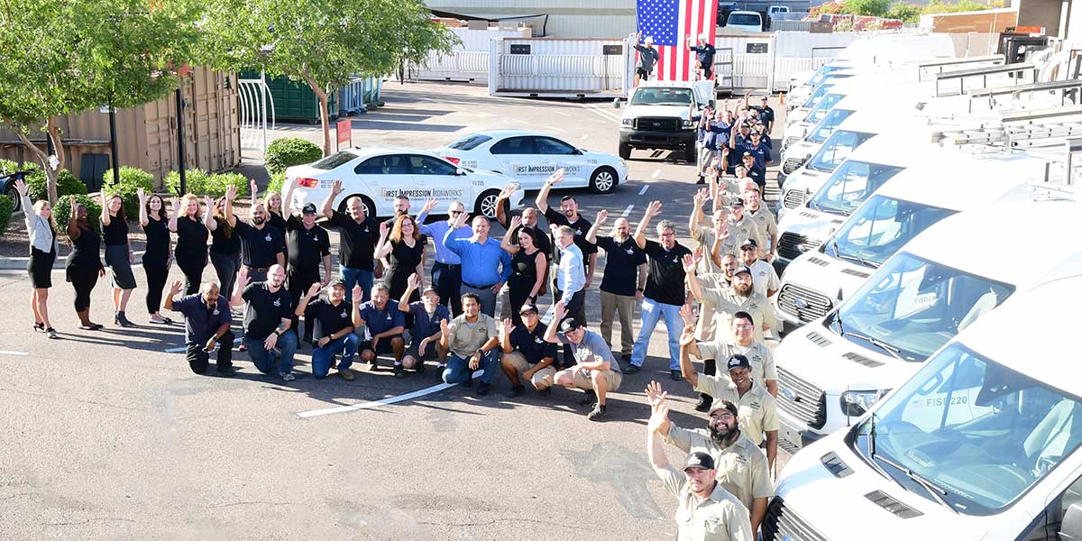 First Impression Ironworks employees gathered in a parking lot, waving