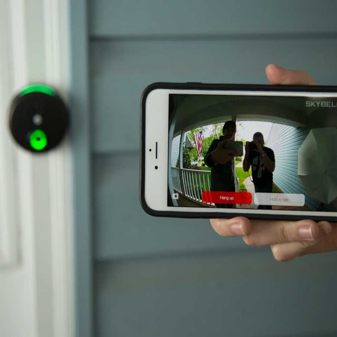 hand holding a phone, showing an image being displayed from the video doorbell in the background 