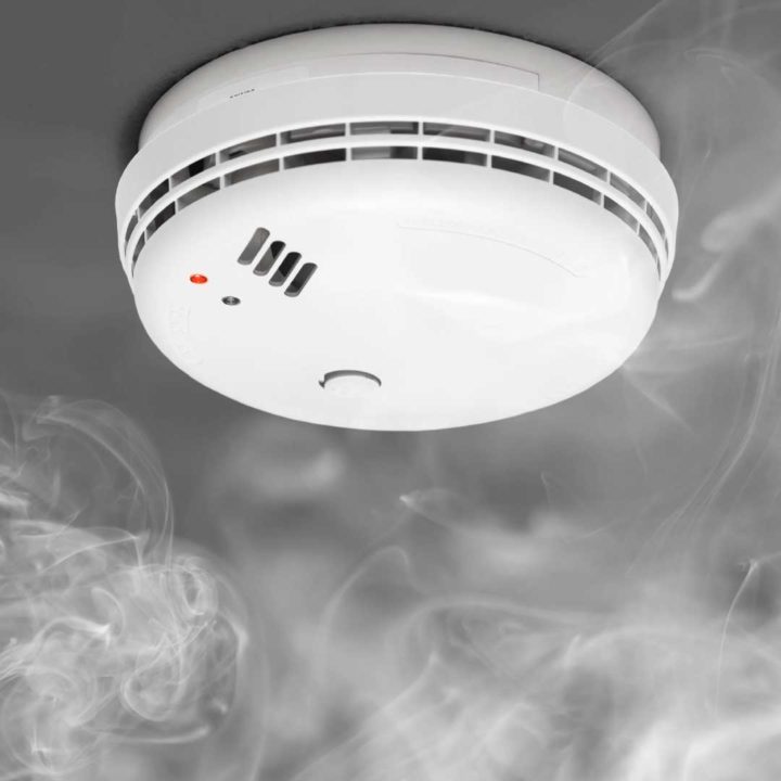 close up image of a smoke detector with smoke hanging around it