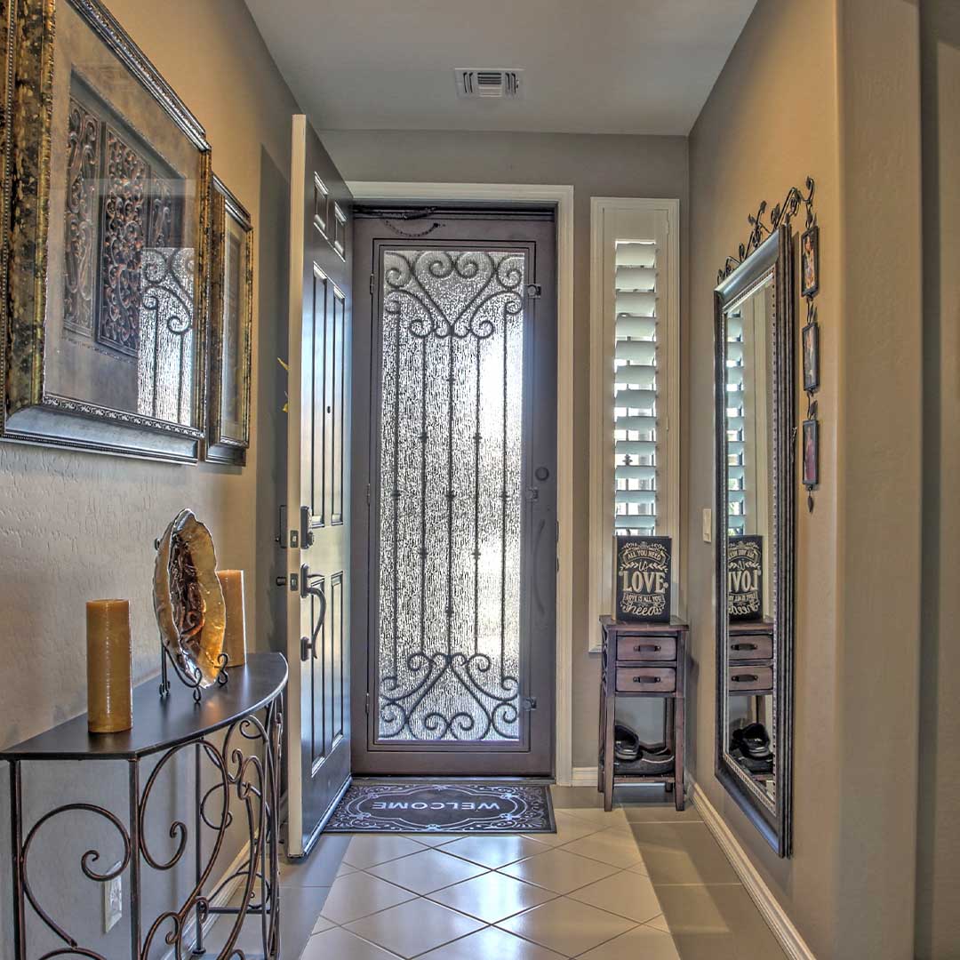 Image looking out the front doors of a home. The interior wooden door is open, swinging into the inside of the home.  The second iron and glass First Impression Ironworks security door is open and swung outward.