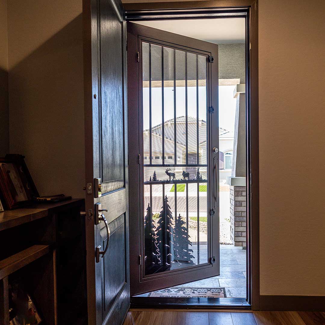 Image looking out the front doors of a home. The interior wooden door is open, swinging into the inside of the home.  The second iron security door is open and swung outward.