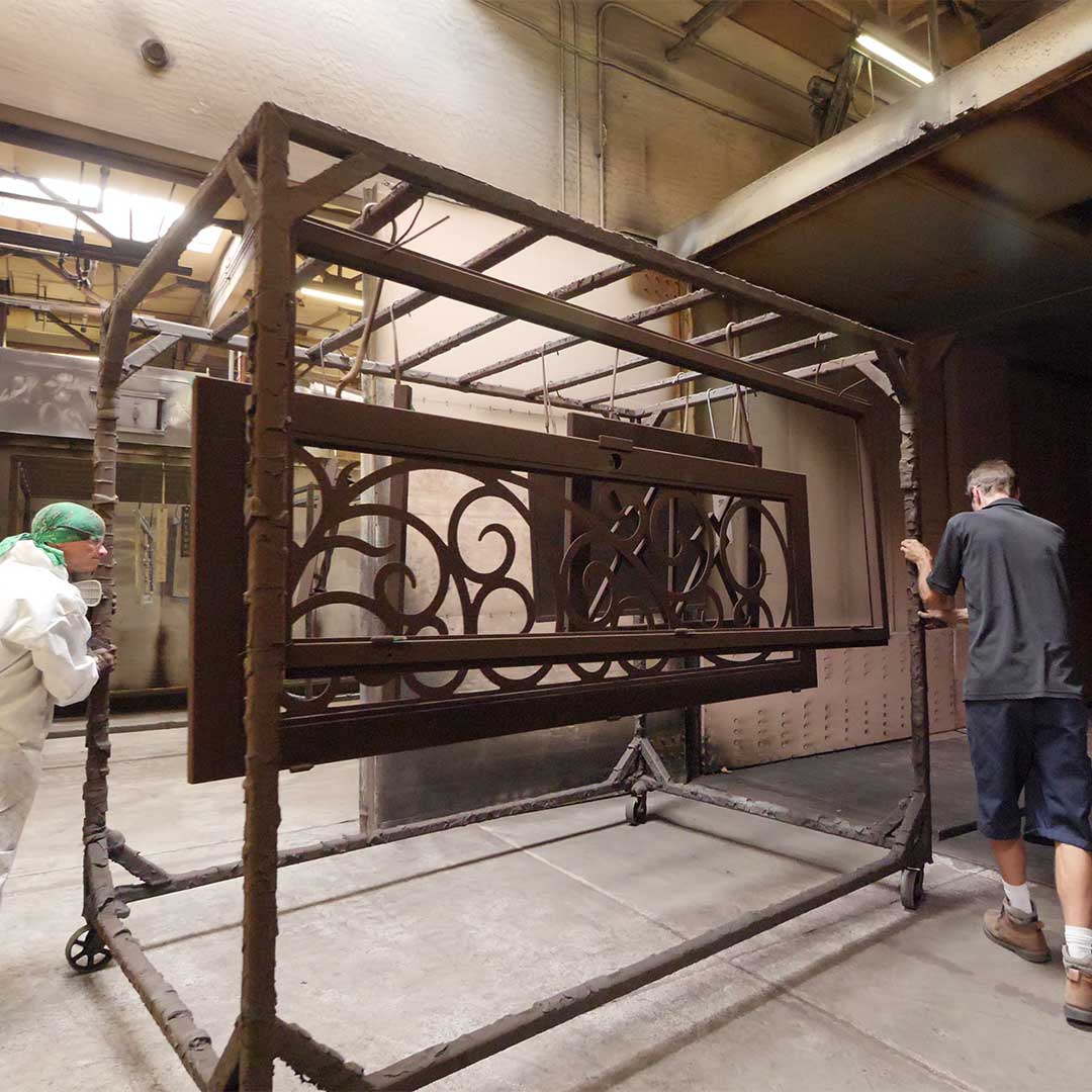 First Impression Ironworks employees wheeling a iron door into the powder coating booth