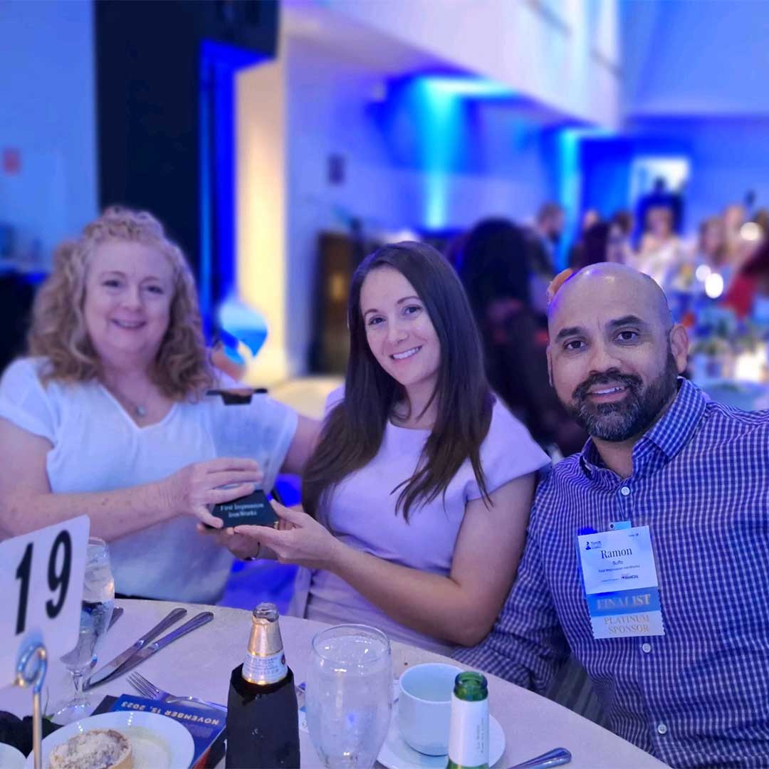 Three First Impression Ironworks team members sitting at a table holding the First Impression Ironworks BBB Torch Award Finalist award