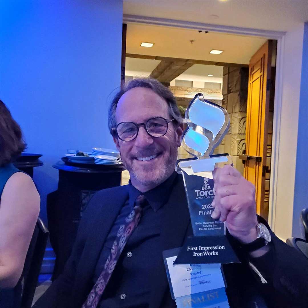 A First Impression Ironworks team members smiling while sitting at a table holding the First Impression Ironworks BBB Torch Award Finalist award