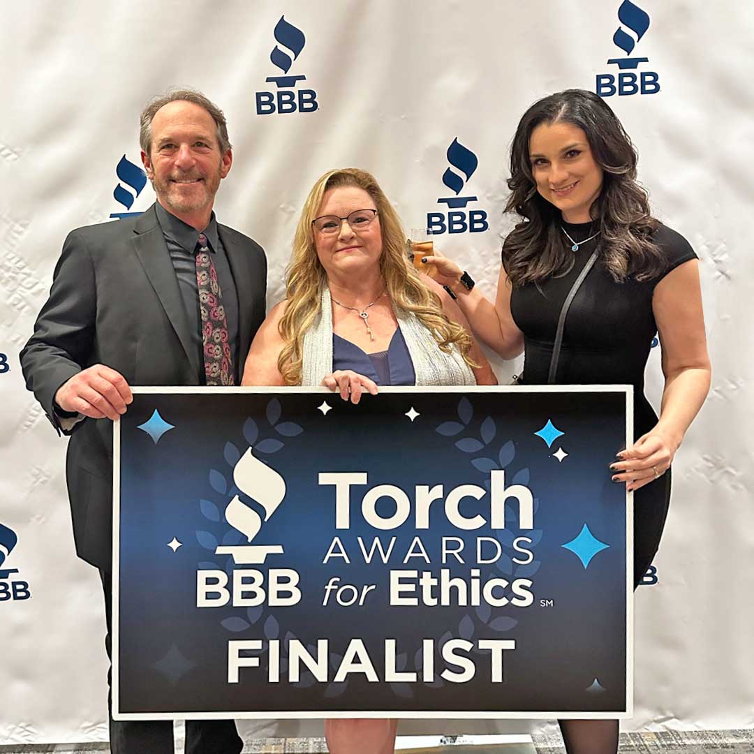 Three First Impression Ironworks team members holding up a sign that reads "BBB Torch Award for Ethics Finalist"