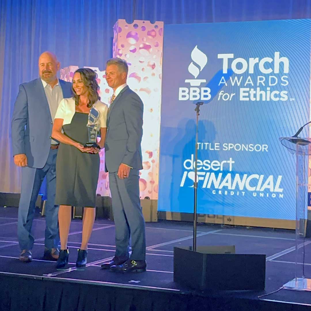 Three senior members of the First Impression Ironworks team standing on stage holding their BBB Torch Award Finalist award