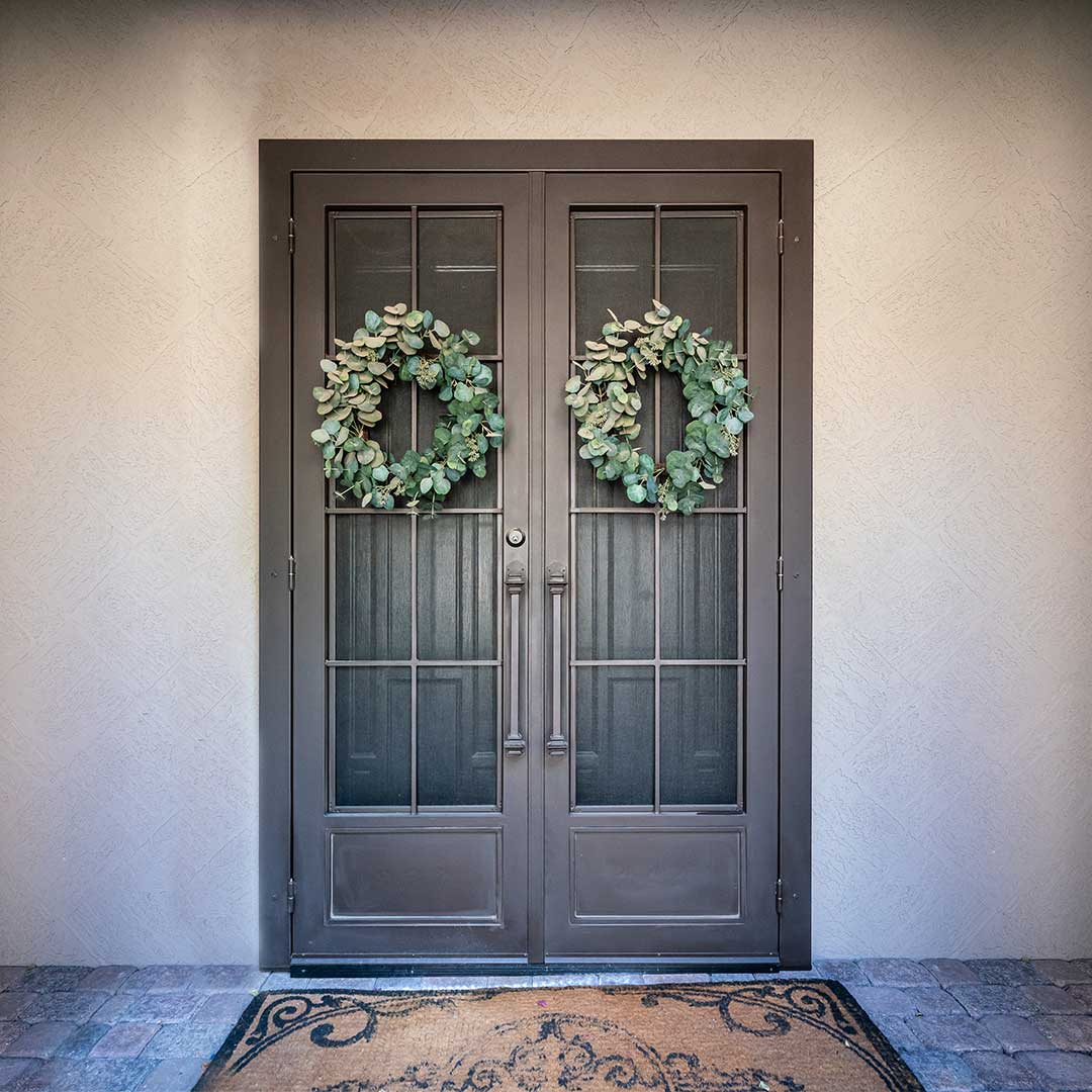 First Impression Ironworks French double iron security doors with a green wreath hung on each door