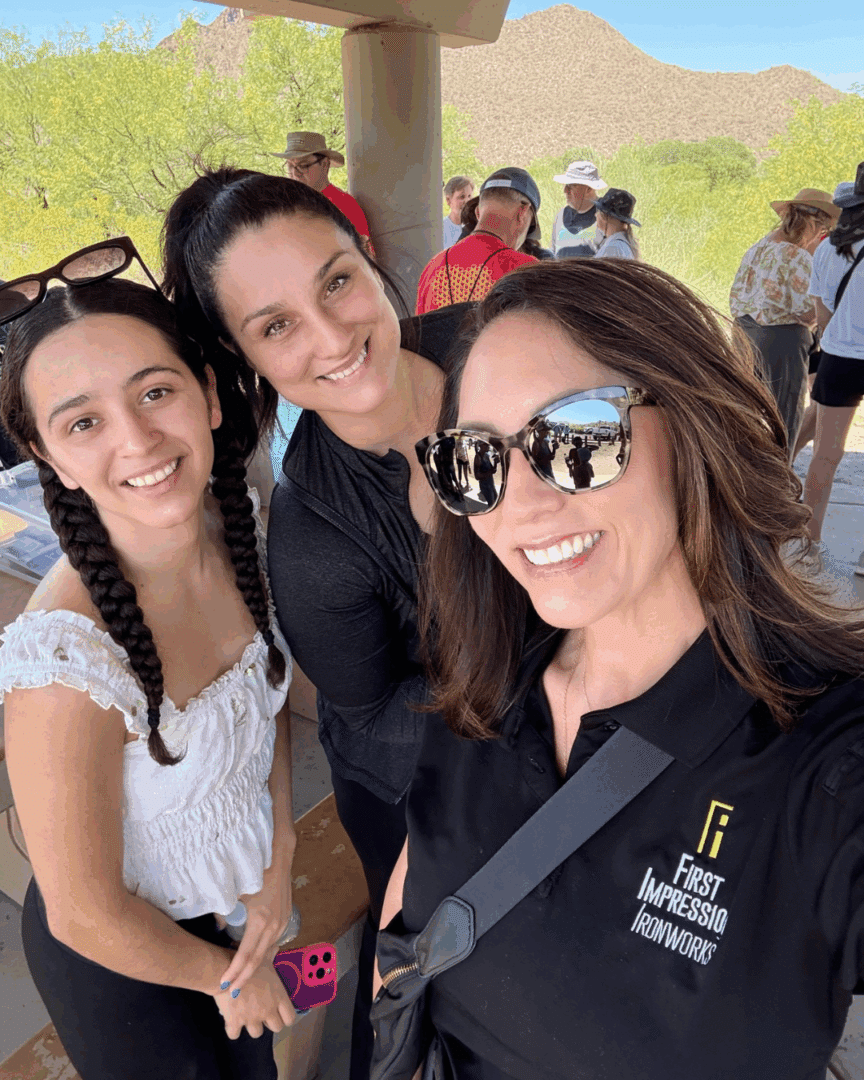 Three women who are First Impression Ironworks employees, smiling at the camera