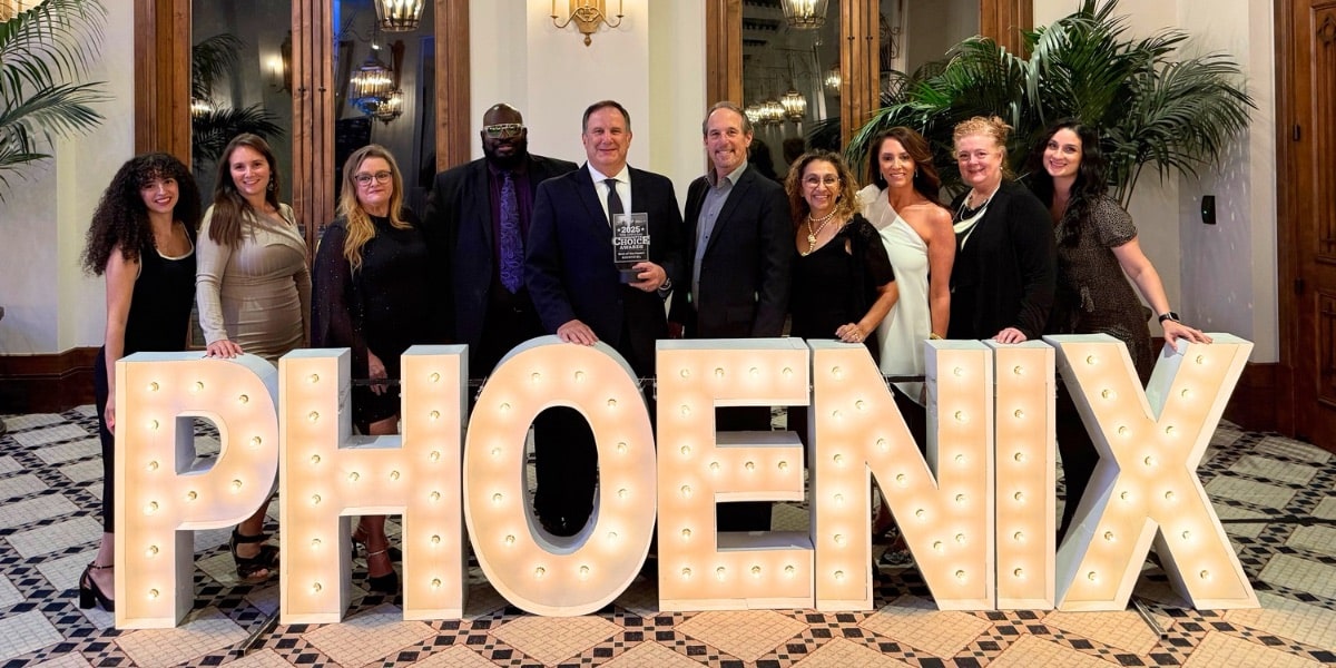 10 members of the First IMpression Ironworks team standing behind marquee letters that spell out "PHOENIX" and the Best of the Desert Awards gala