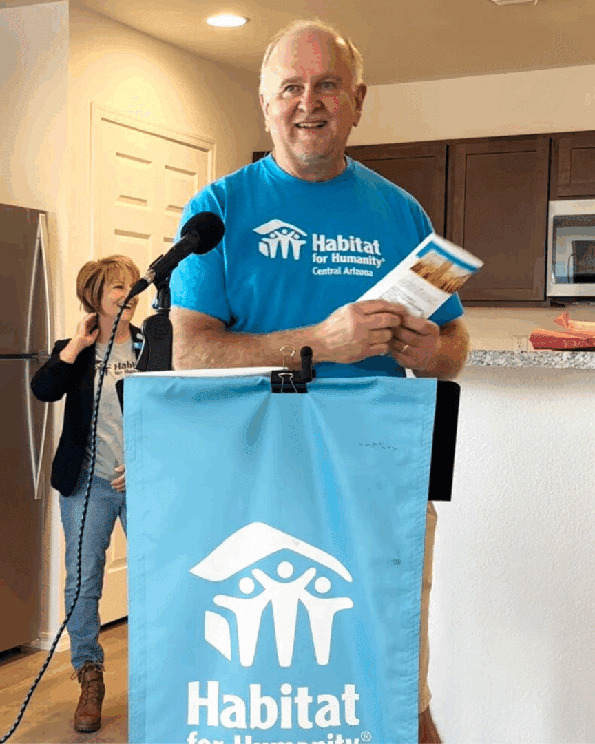 A member of the Habitat for Humanity team, standing at a podium, making a speech about the home that was just build for a single mother
