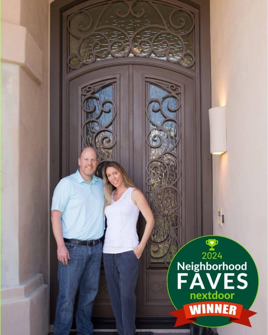 Husband and wife smiling in front of their gorgeous First Impression Ironworks iron and glass entry door