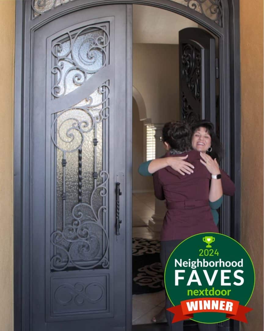 Two happy women hugging in the doorway of a large First Impression Ironworks entry door