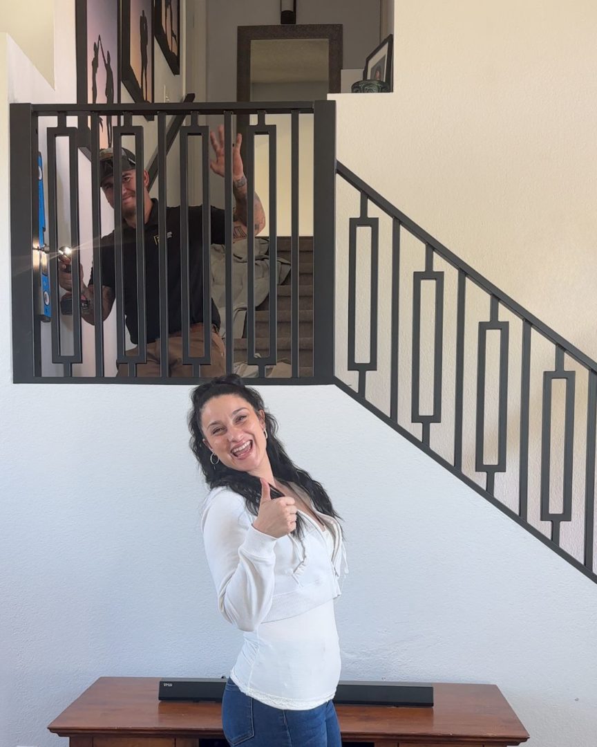 Homeowner smiling and giving a thumbs up in front of her new First Impression Ironworks iron railing