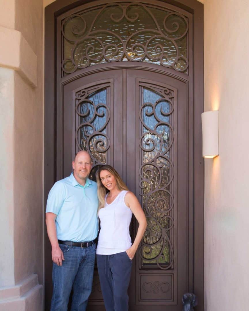 Two people smiling in front of their custom Iron Entry Door by First Impression Ironworks