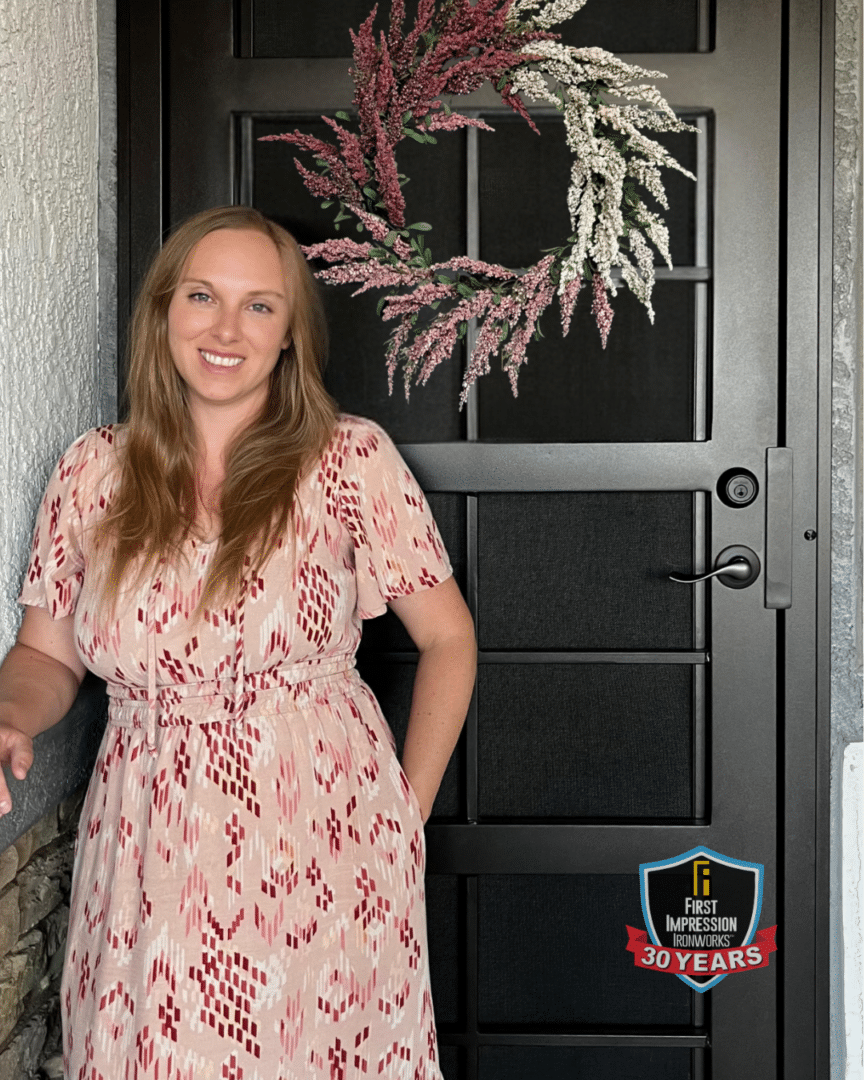 Smiling woman posing for a picture in front of her First Impression Ironworks iron entry door